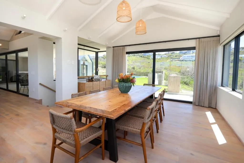 Dining table for eight under raffia pendant lights, sliding doors open to a garden and hillside view