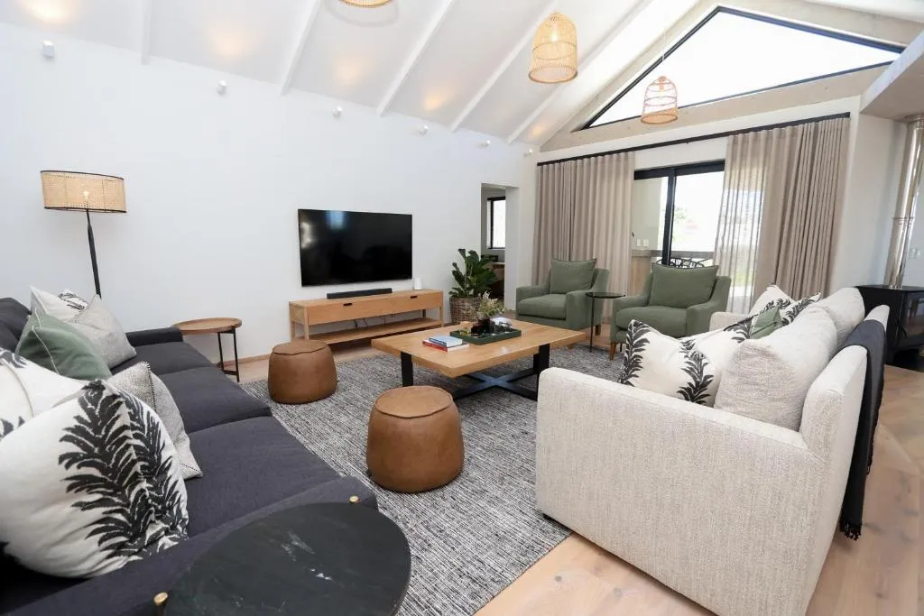 Open-plan lounge with vaulted ceiling, sectional sofas and armchairs facing a wall-mounted TV
