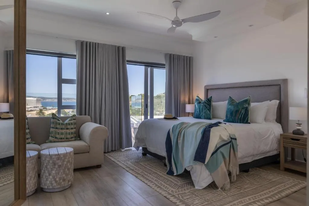 Bedroom with a ceiling fan and floor-to-ceiling windows framing the bay and hillside beyond