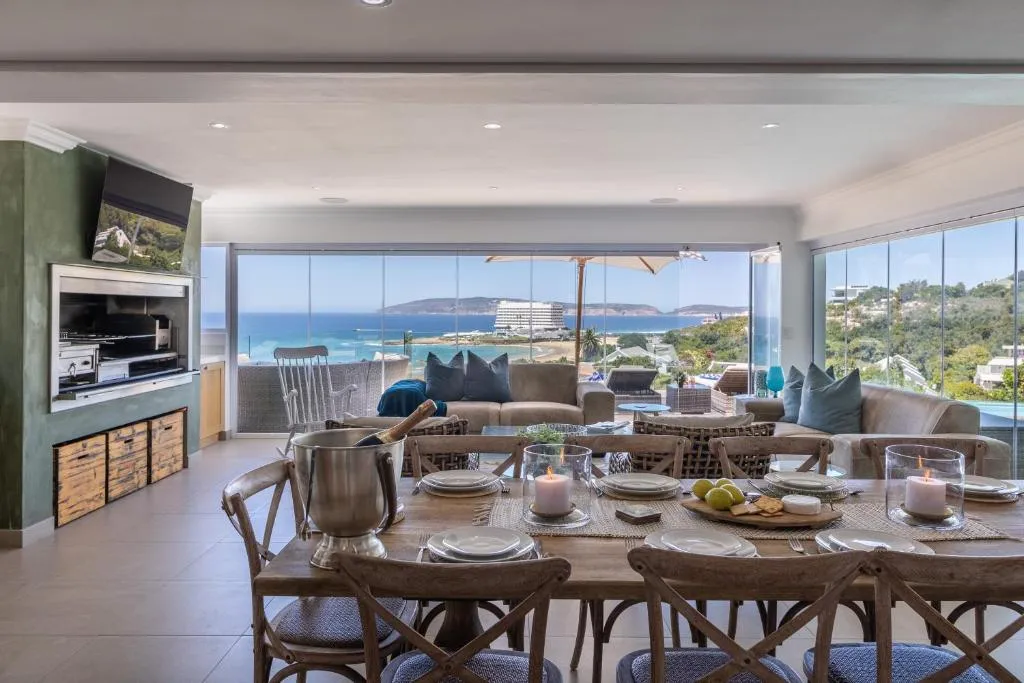 Outdoor dining terrace with a built-in braai and glass walls open to the ocean and headland