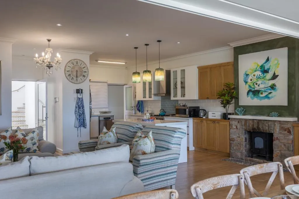 Open-plan living and kitchen area with a chandelier, striped sofas and a stone-clad wood fireplace