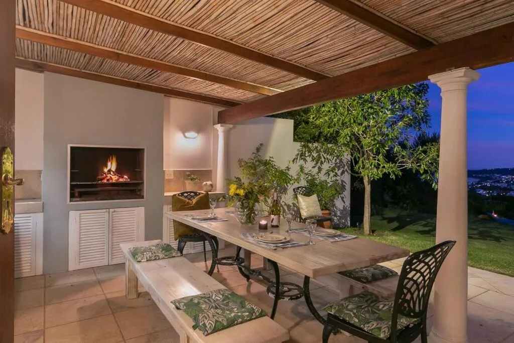Covered braai patio with a lit fire, a long dining table and a view over the town at dusk
