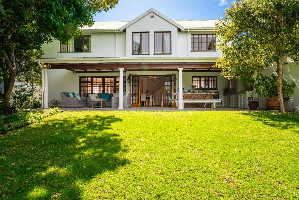 Cape-style house exterior with a covered patio, outdoor dining table and a wide lawn