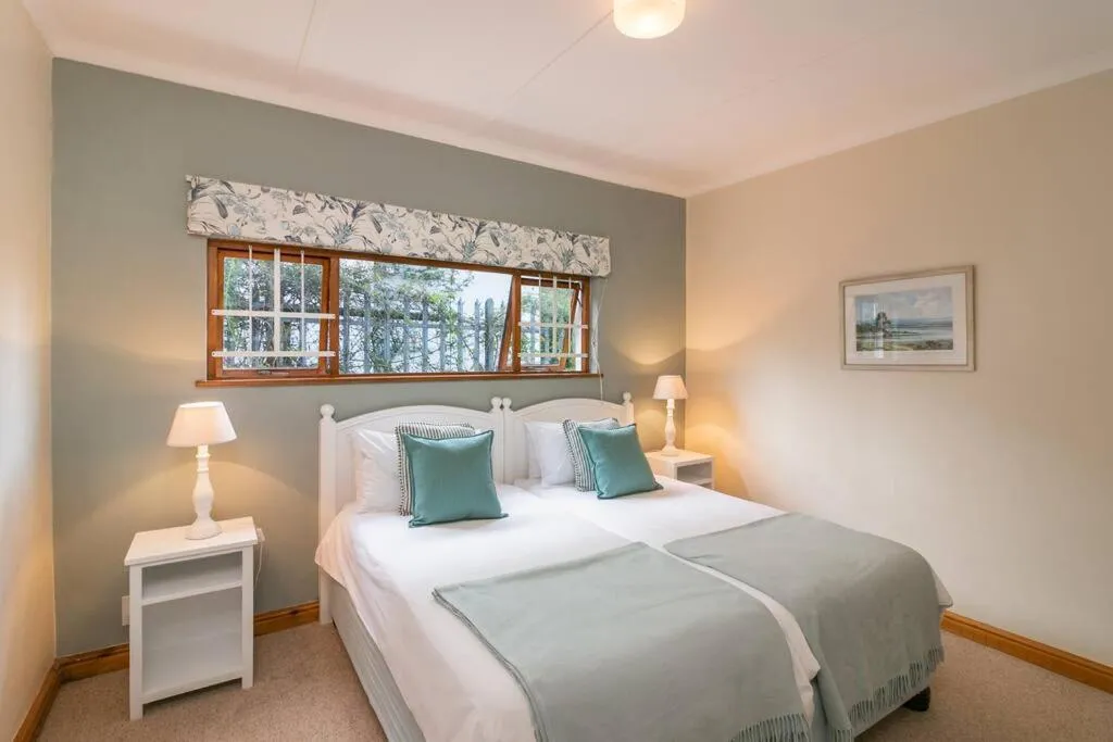 Twin bedroom with sage-green throws and a window looking onto a fenced garden