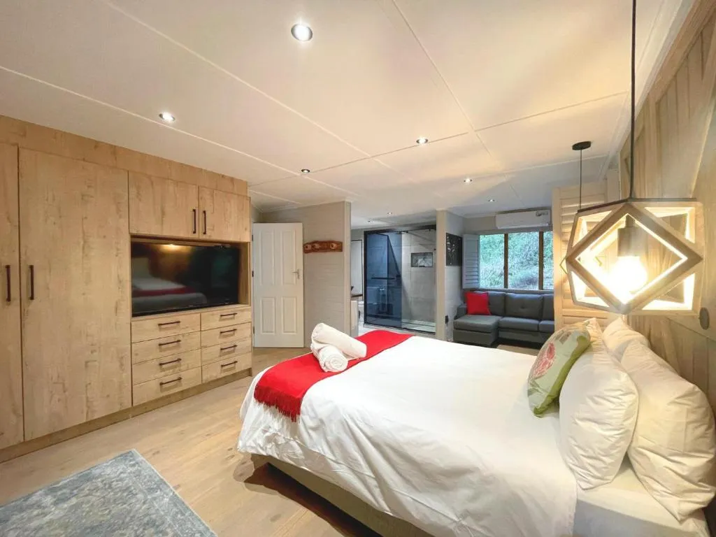 Second bedroom with a built-in wardrobe and TV unit, red throw, and a forest-facing window