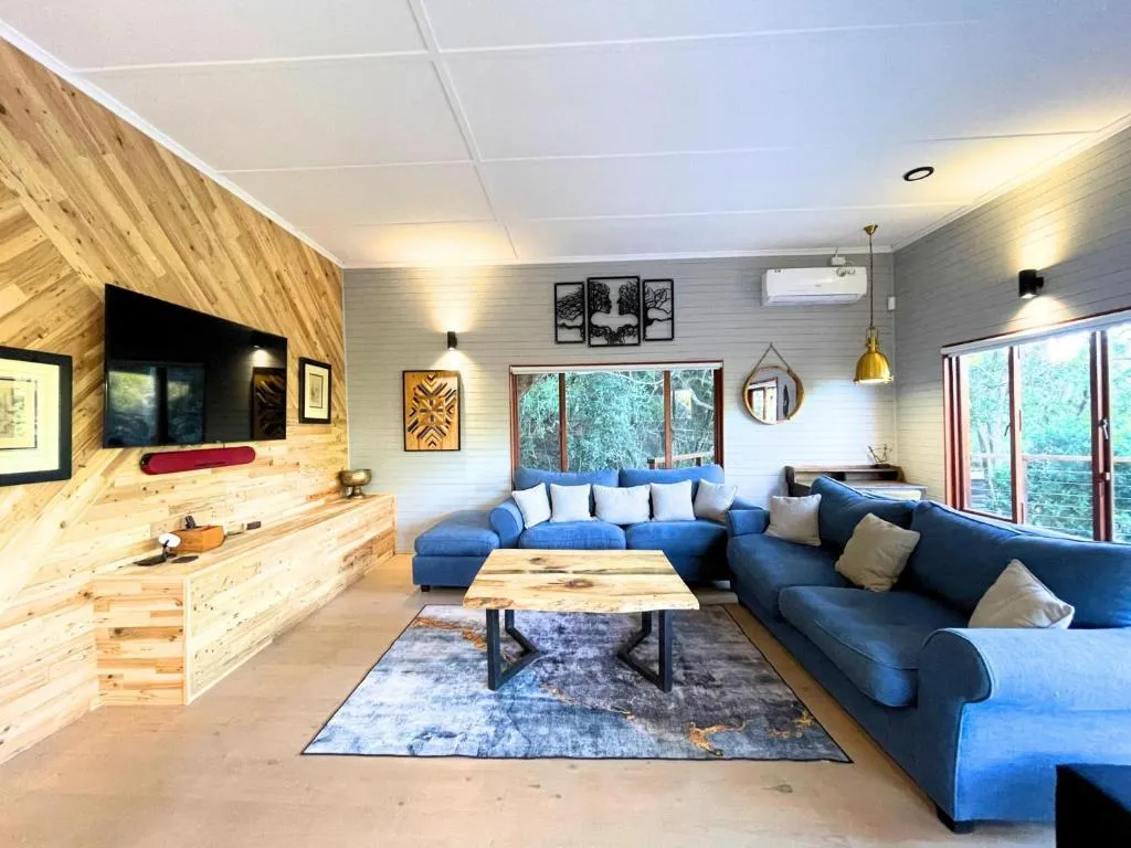 Living room with a blue sectional sofa, wood-panel TV wall, and windows onto the forest