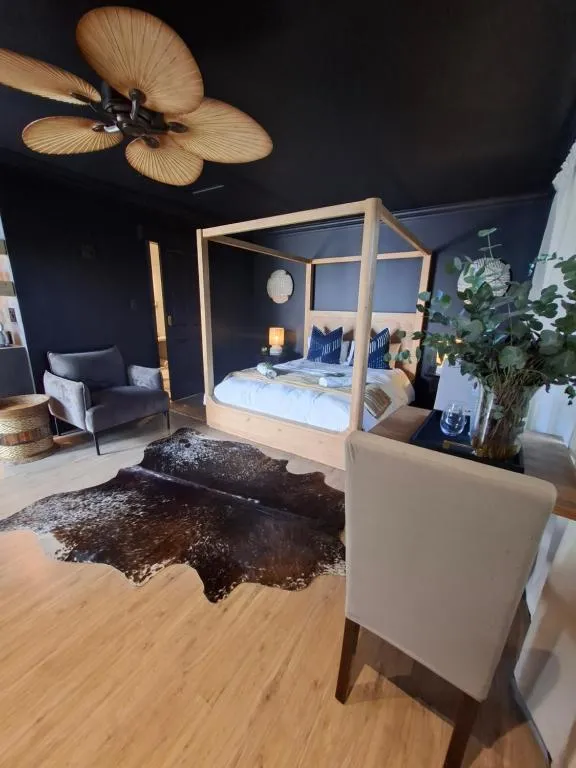 Four-poster wooden bed in a dark-walled cabin room with a cowhide rug and lounge chair
