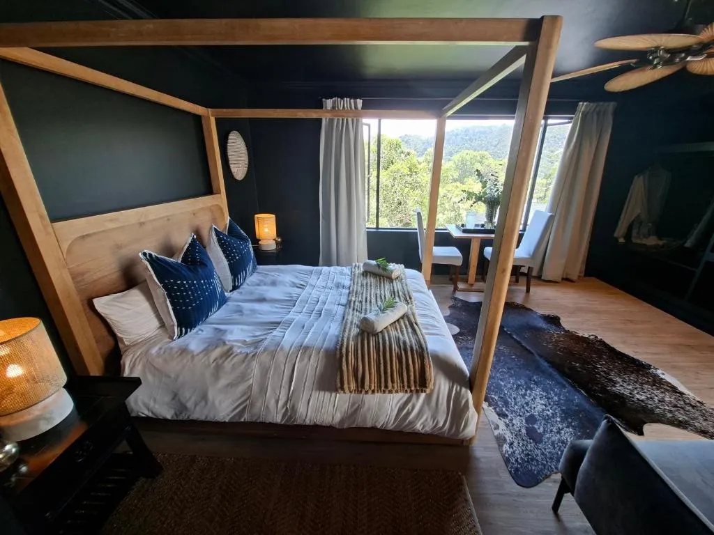 Four-poster bed positioned to face a window framing forest and hillside views