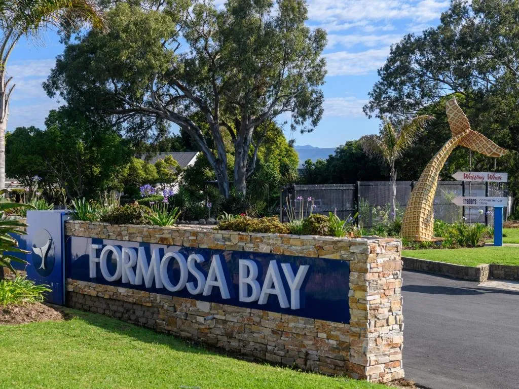 Formosa Bay entrance sign built into a stone wall with a driftwood whale-tail sculpture
