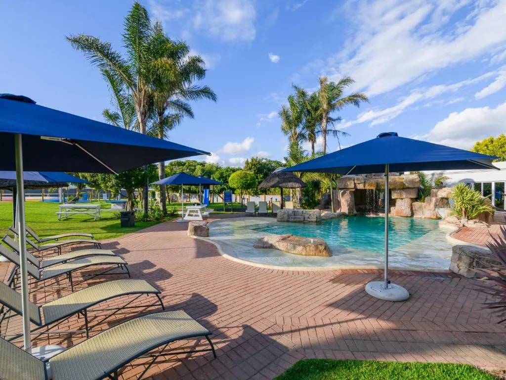 Pool deck with blue umbrellas and loungers beside a rock-edged swimming pool