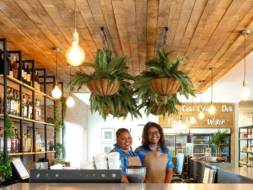 Resort deli and bar counter with hanging fern baskets and staff serving cold drinks