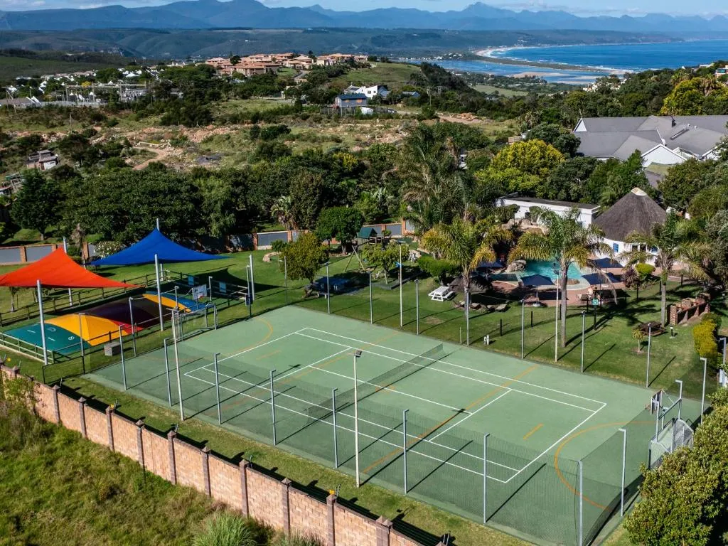 Aerial view of a full-size tennis court with coloured shade sails and a play area alongside