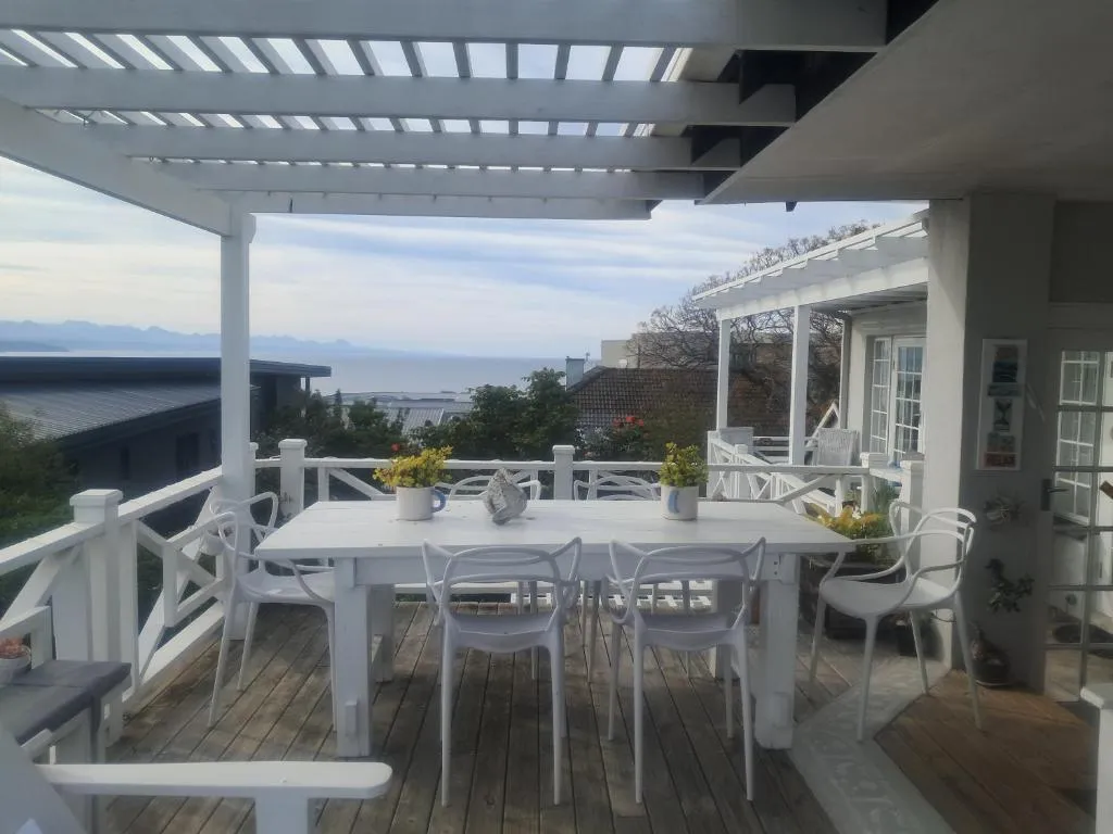 Covered pergola deck with a long white dining table looking out over rooftops to the sea