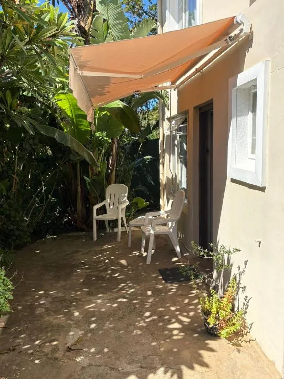 Paved courtyard patio with a retractable orange awning, plastic chairs and banana palms