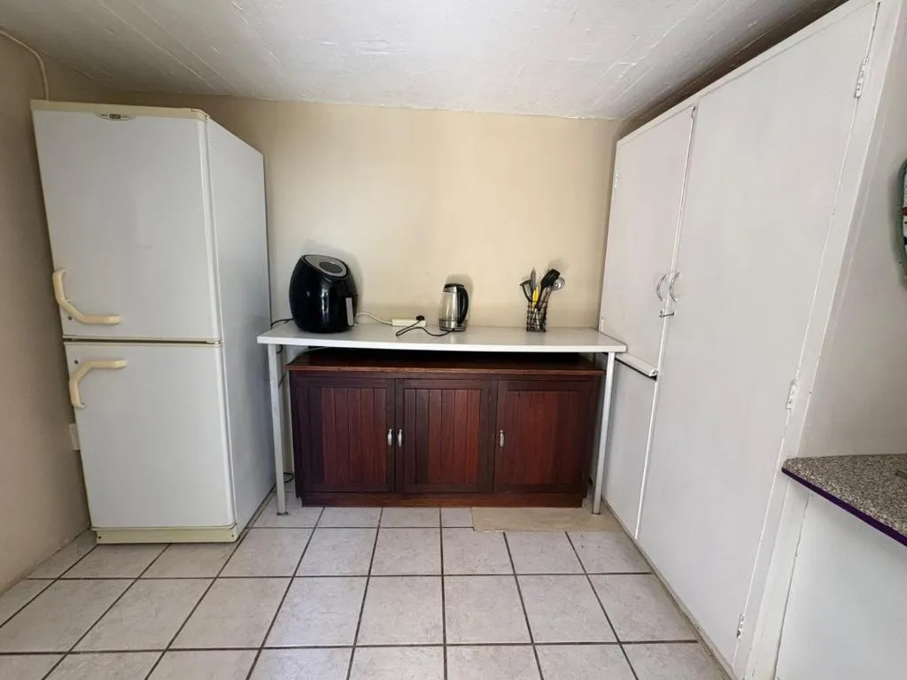 Kitchenette with a white fridge, air fryer, kettle and a dark wood cupboard on tiled flooring