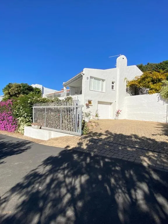 Street view of the white double-storey house with a wrought-iron gate and bougainvillea hedge