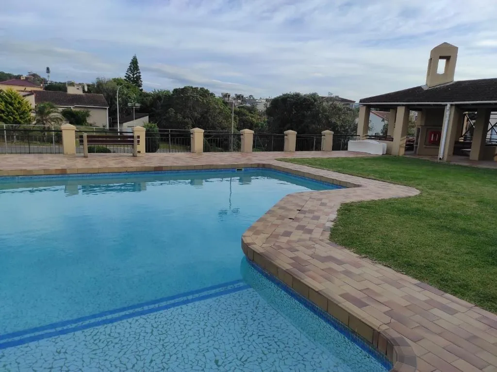 Shared complex pool with paved surround, lawn and a lapa beyond the fence line