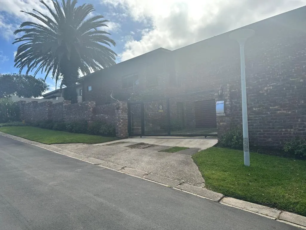 Brick house exterior with a tall palm tree beside the gated driveway entrance