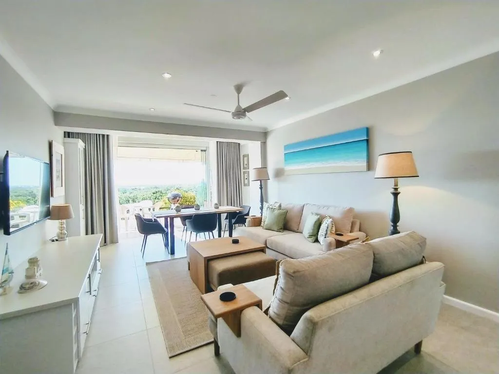 Living room with sea-themed art, ceiling fan and a dining table opening onto the balcony