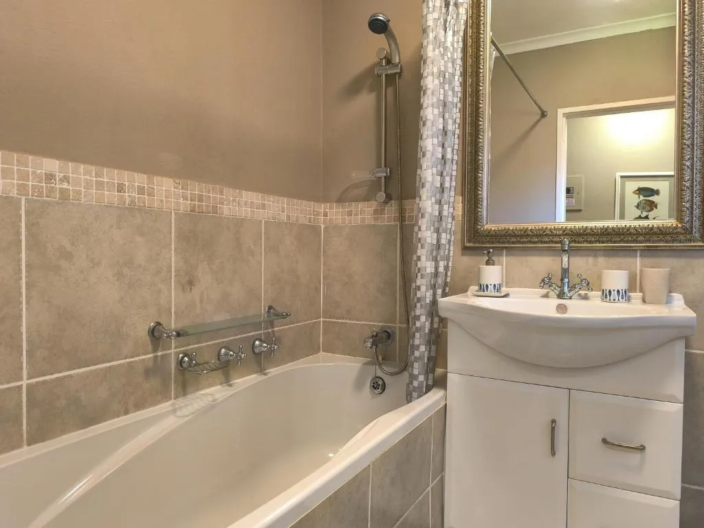 Bathroom with a corner bath, mosaic tile trim and a gold-framed mirror above the vanity
