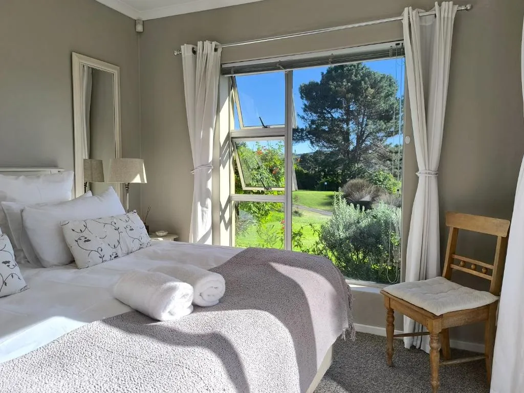 Bedroom with a garden view through full-length windows and folded towels on the turned-down bed
