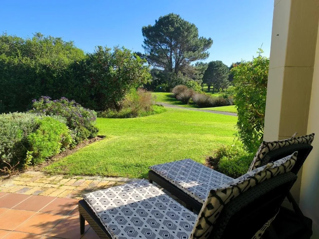 Private patio with cushioned loungers overlooking a lawn and path framed by fynbos planting
