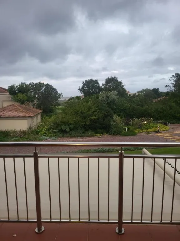 Balcony with steel railing overlooking shrubland and estate grounds under an overcast sky