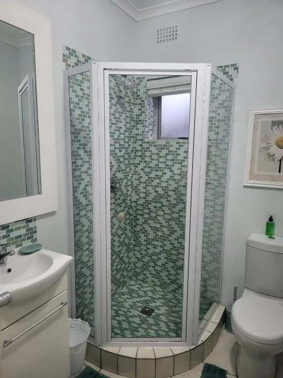 Corner shower bathroom with green mosaic tile and a pedestal basin
