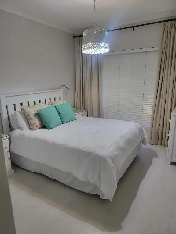 Bedroom with white slatted headboard, teal cushions and a pendant light fixture