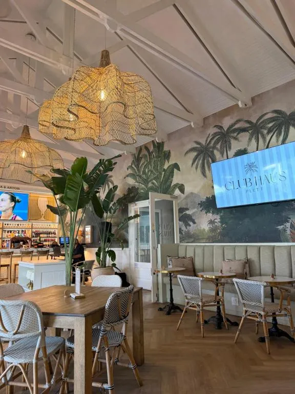 Club Haus Plett clubhouse restaurant with palm-leaf mural and bar seating