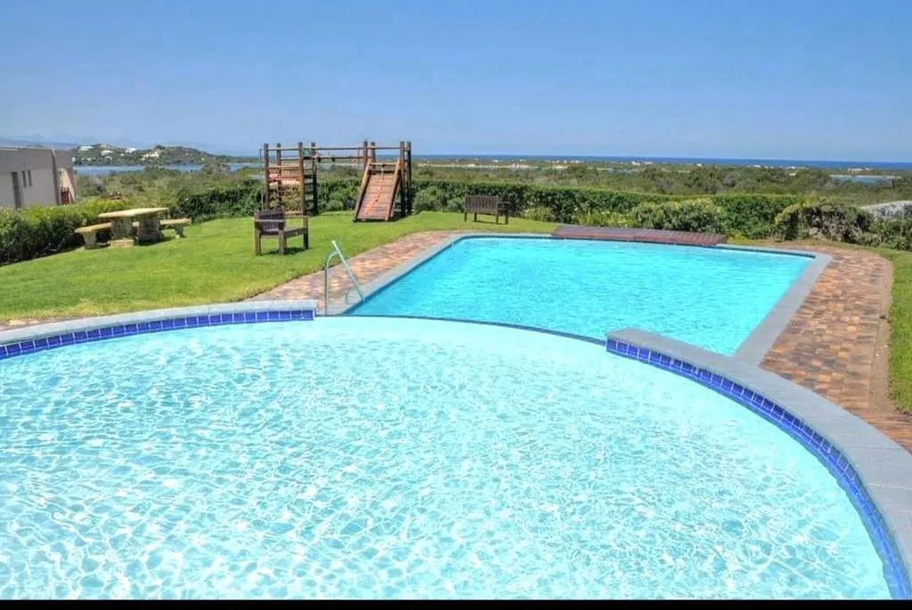 Two connected swimming pools with a children's climbing frame and a distant sea view