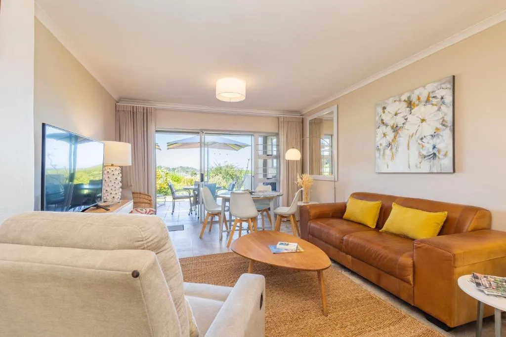 Living room with a tan leather sofa, yellow cushions and a glimpse of the patio beyond