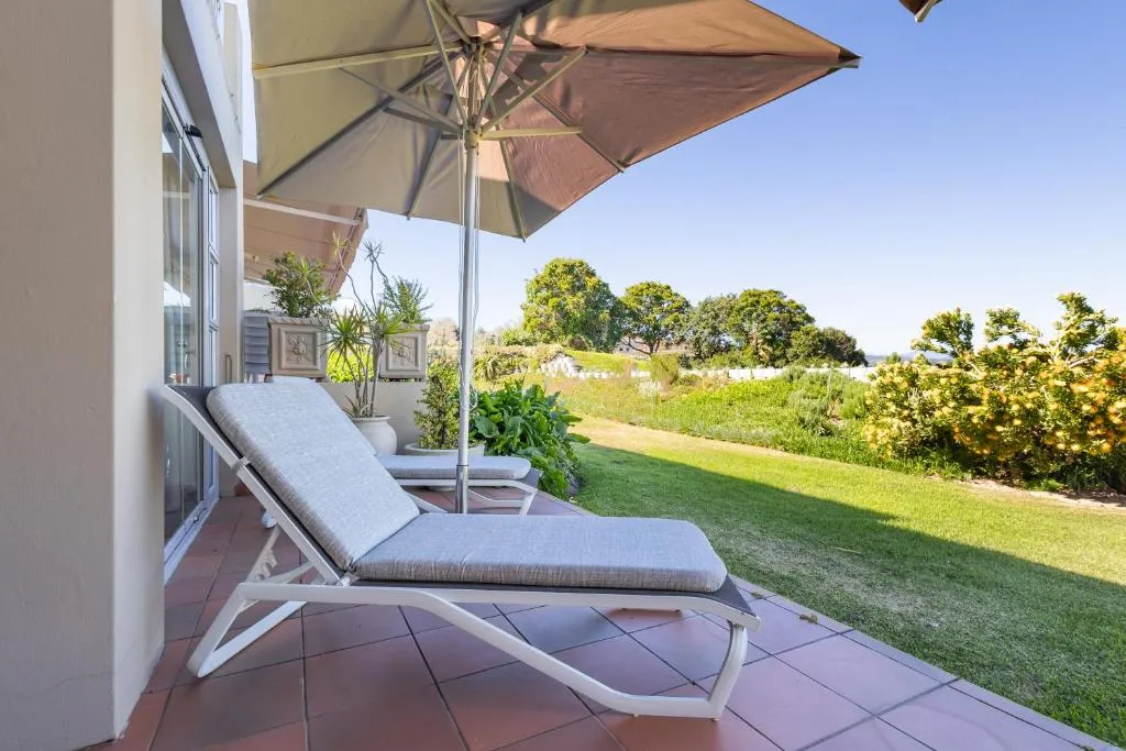 Sun lounger on a shaded terrace beside potted plants and garden beds