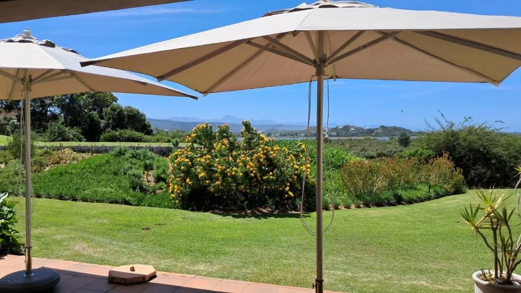 Terrace umbrellas framing flowering shrubs, lawn and a distant lagoon and hills