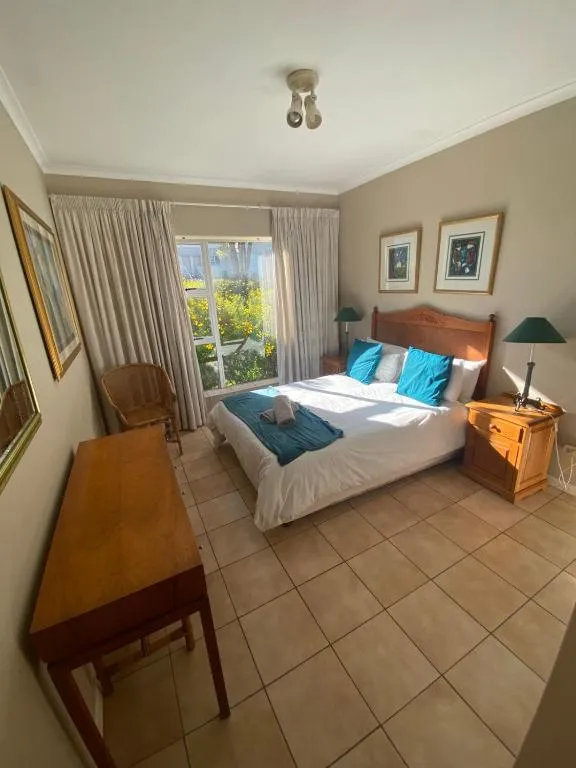 Main bedroom with teal scatter cushions and a sliding door onto a flowering garden view