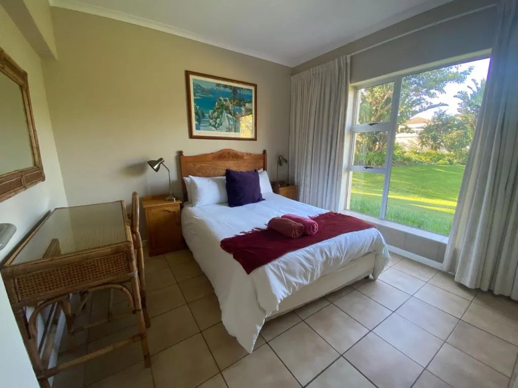 Second bedroom with a queen bed, maroon throw and a garden and lawn view through the window