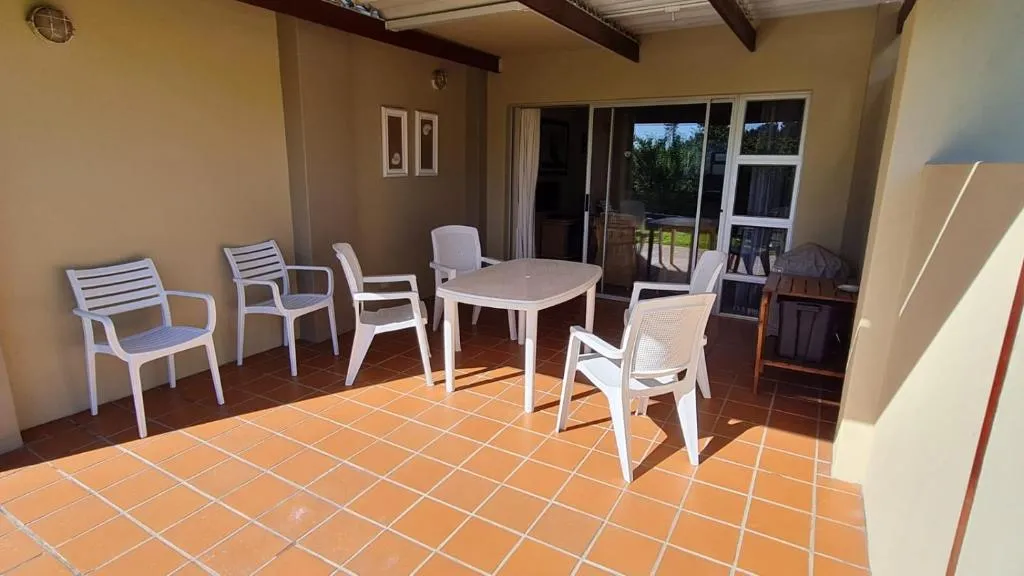 Covered patio with a white outdoor dining table, six chairs and sliding doors to the lounge