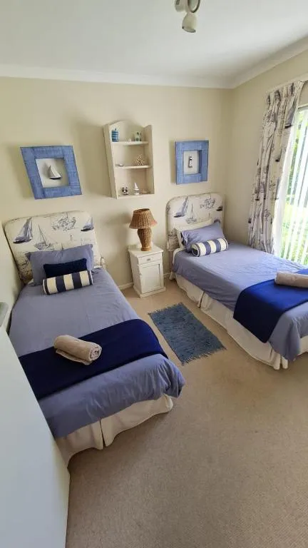 Twin bedroom with nautical-themed decor, matching blue bedspreads and beach-style artwork