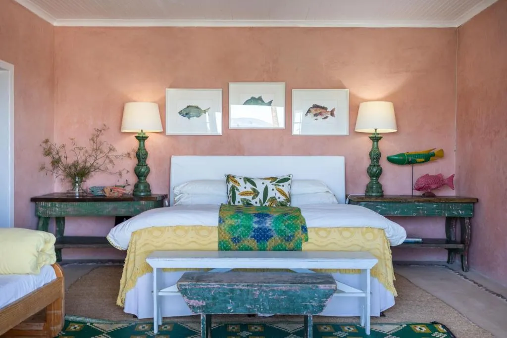 Bedroom with pink limewashed walls, twin bedside lamps and framed fish prints above the headboard