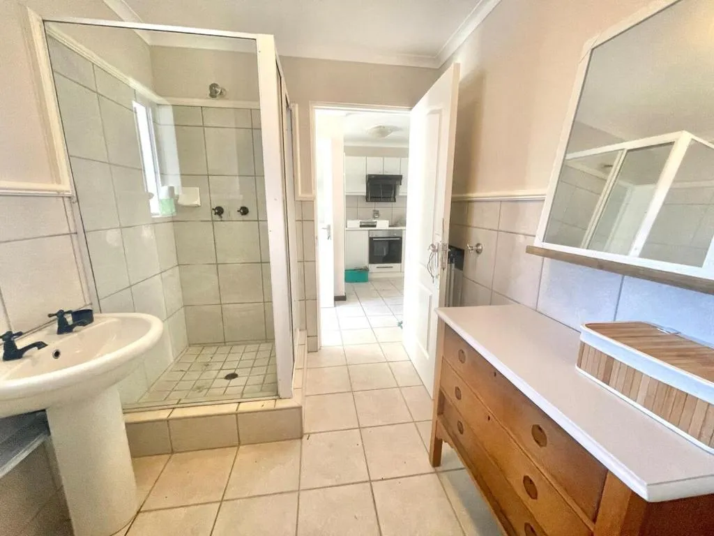 Tiled shower room with a pedestal basin, wall mirror and a doorway opening onto the kitchen