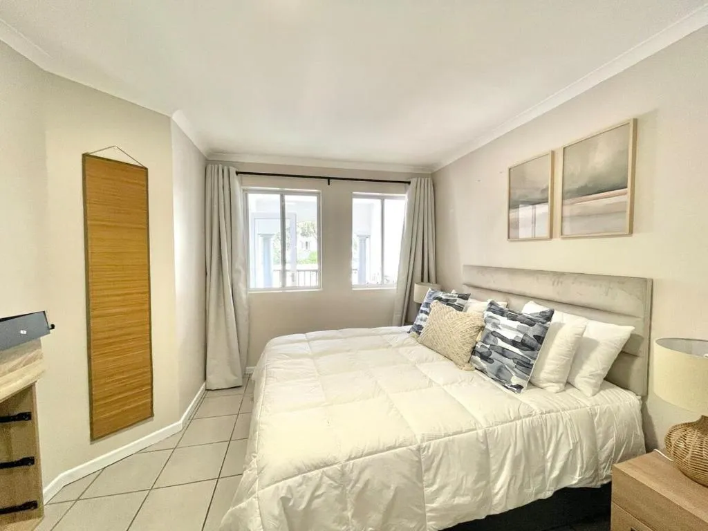 Bedroom with a white bed, patterned cushions, wardrobe cabinet and a curtained window onto the balcony