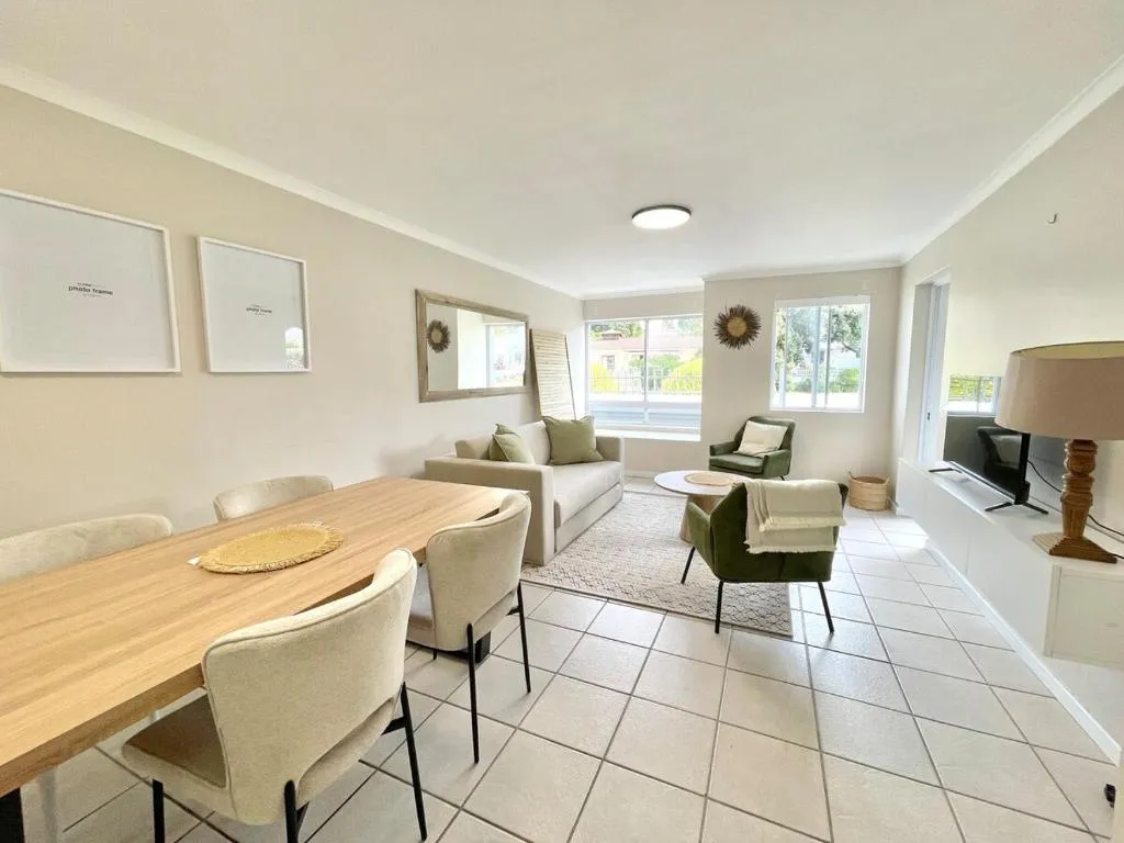 Open-plan dining area with a wooden table for four beside the lounge seating and television