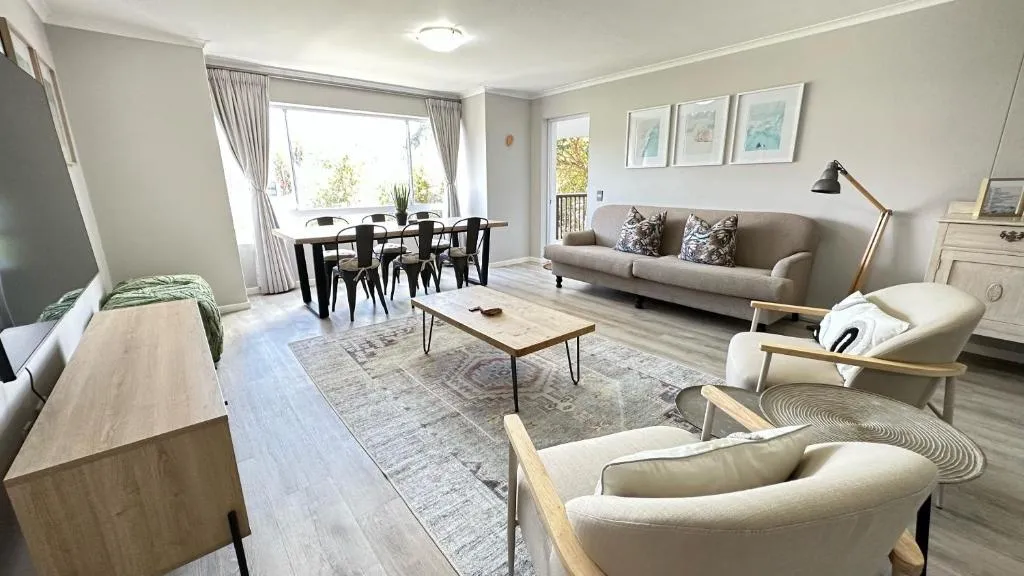 Open-plan lounge and dining area with a grey sofa, armchairs and a four-seat table by the window