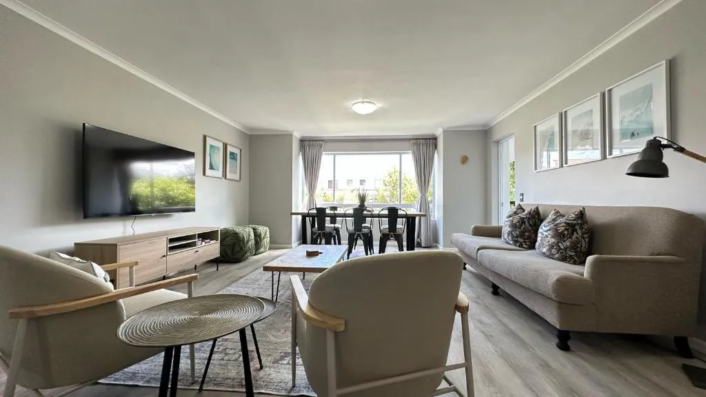 Second view of the lounge with a wall-mounted TV, armchairs and the dining table beyond