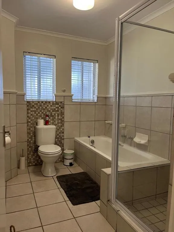 Bathroom with a corner shower, built-in bathtub and mosaic-tiled feature wall behind the toilet