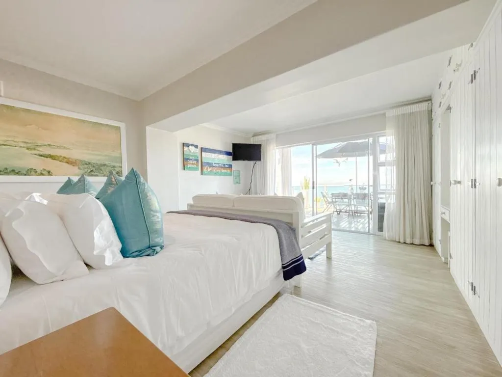 Bed with teal cushions facing sliding doors that open onto a sea-view balcony