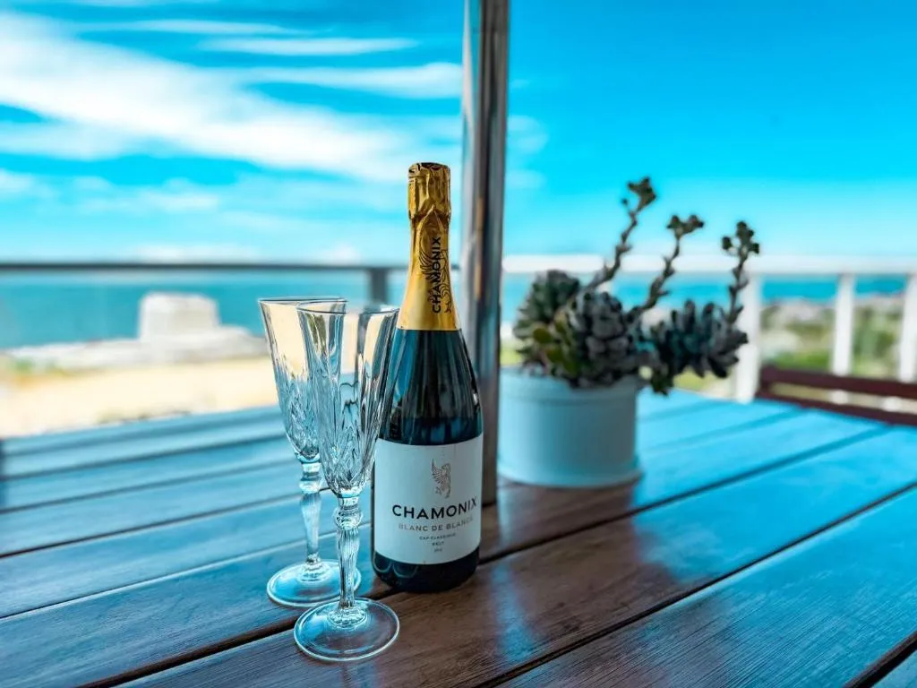Champagne bottle and glasses set on the deck table with the ocean blurred in the background