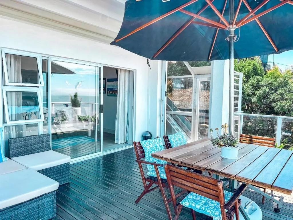 Private deck with a wooden dining table, blue umbrella and rattan seating overlooking the ocean