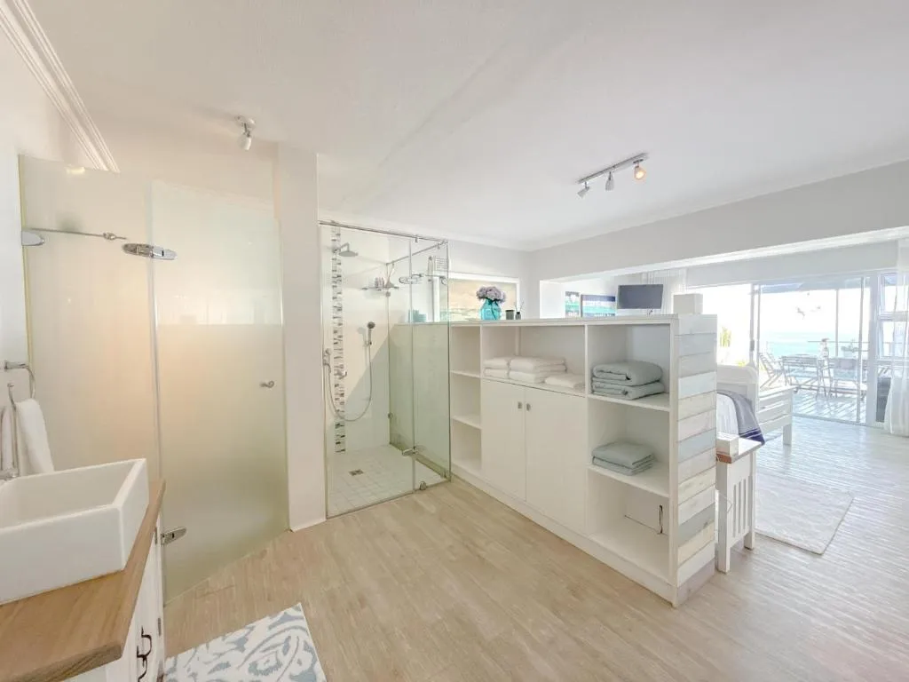 Open-plan ensuite bathroom with a glass shower and floating vanity beside the sea-facing deck
