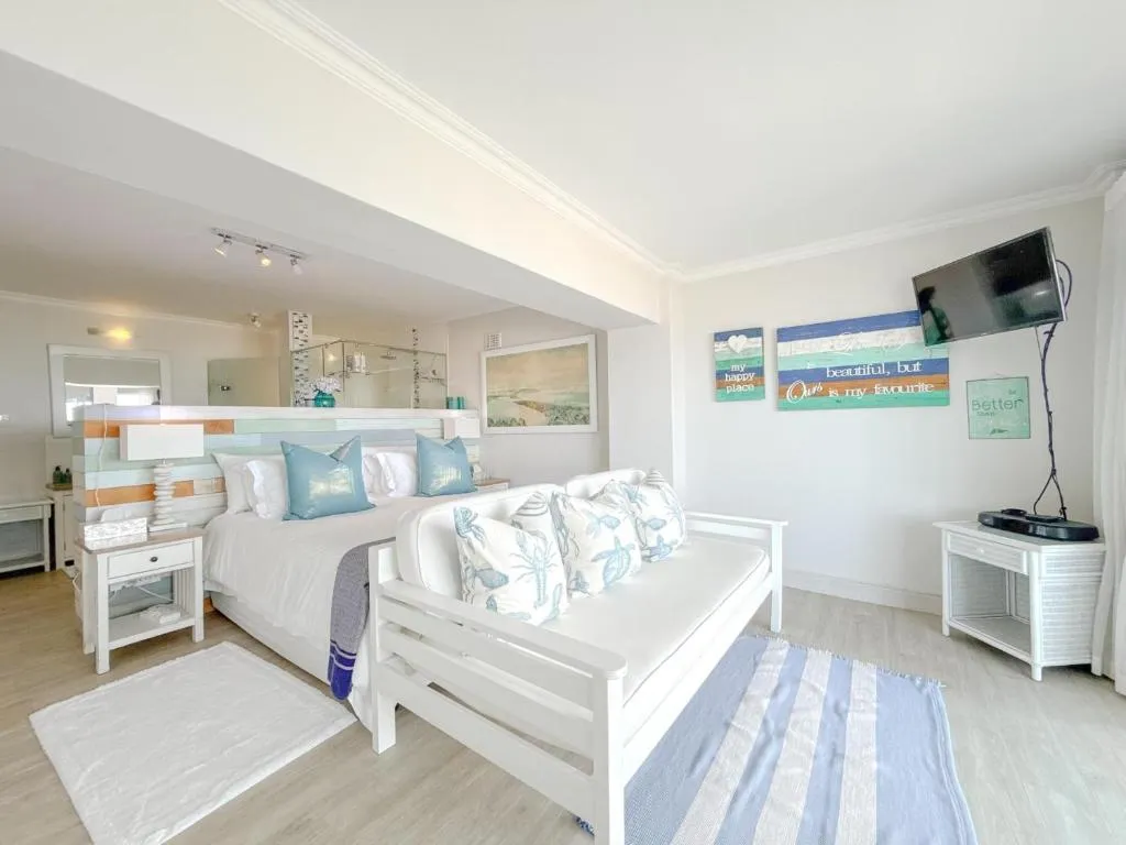 Studio bedroom with a white daybed sofa, beach-theme wall art and a wall-mounted TV